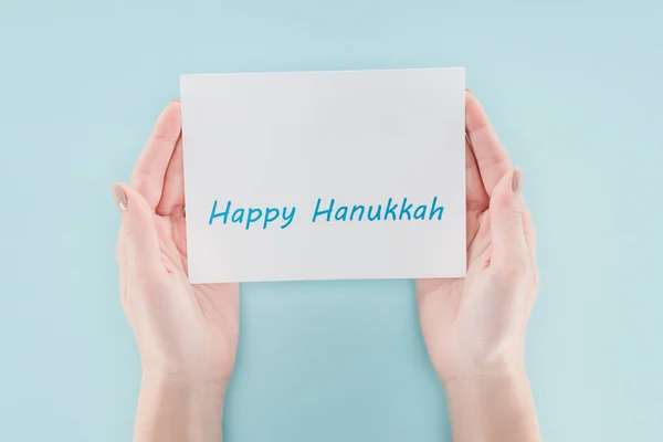 Corte tiro de mulher segurando cartão com feliz hannukah lettering no fundo azul, hannukah conceito — Fotografia de Stock