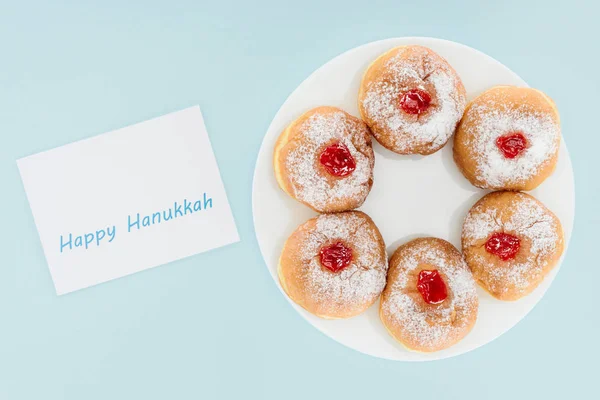 Vista superior de las rosquillas en el plato y feliz tarjeta hannukah aislado en azul, concepto hannukah - foto de stock