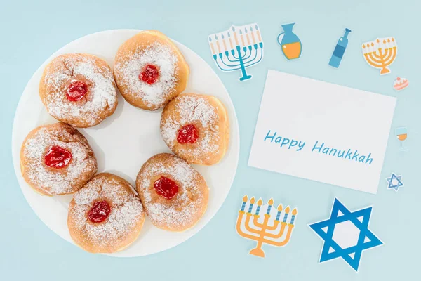 Top view of doughnuts on plate and happy hannukah card isolated on blue, hannukah concept — Stock Photo