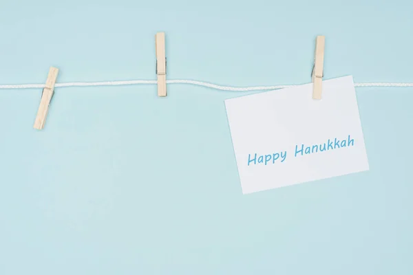 Vue du dessus de la carte heureuse hannukah cloué sur la corde avec des vêtements cheville isolé sur bleu, concept hannukah — Photo de stock