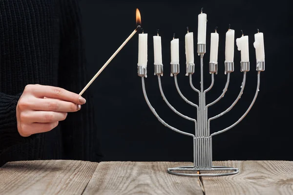 Partial view of woman lighting candles on menorah on wooden tabletop on black backdrop, hannukah holiday concept — Stock Photo