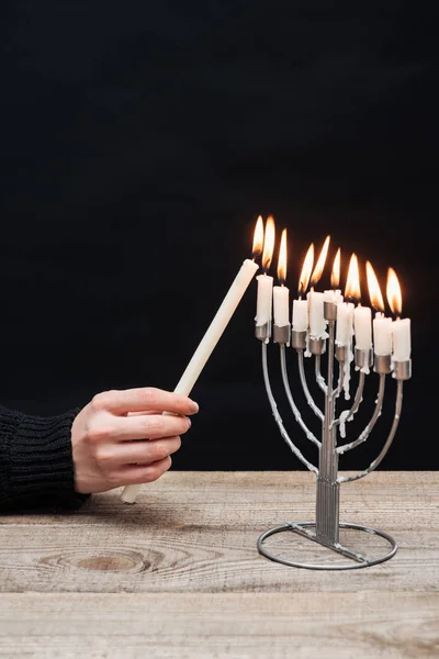 Visão parcial da mulher acendendo velas no menorah na mesa de madeira em pano de fundo preto, conceito de feriado hannukah — Fotografia de Stock