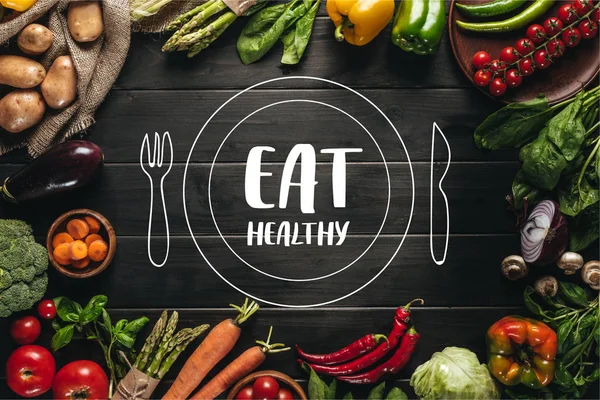 Frame of organic fresh vegetables on sacking on wooden tabletop with eat healthy lettering with drawn plate and cutlery — Stock Photo