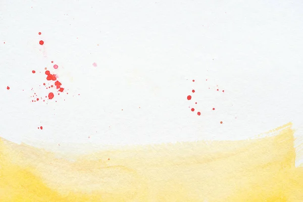 Trait d'aquarelle jaune avec éclaboussures rouges sur fond de papier blanc — Photo de stock