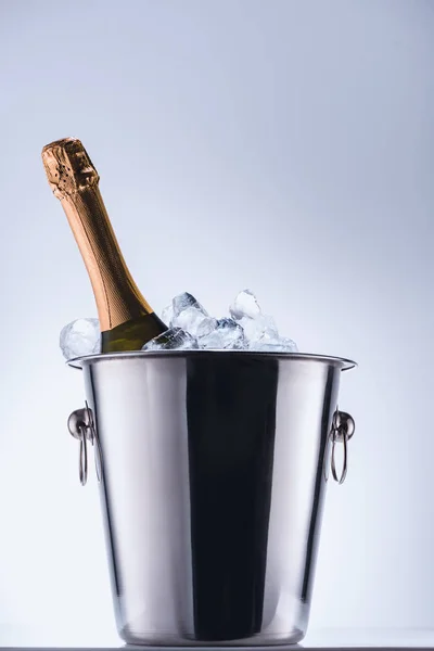 Vista de cerca de la botella de champán en cubo con cubitos de hielo sobre fondo gris - foto de stock