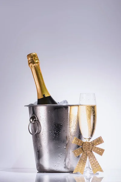 Close up view of bottle of champagne in bucket and glass of champagne on grey backdrop — Stock Photo