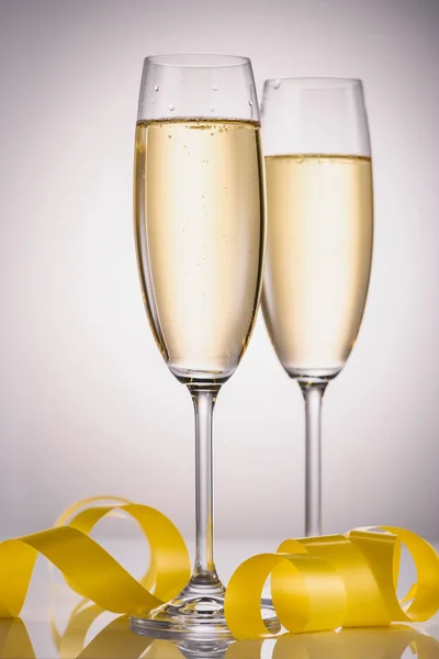 Close up view of glasses of champagne and yellow festive confetti on grey background — Stock Photo