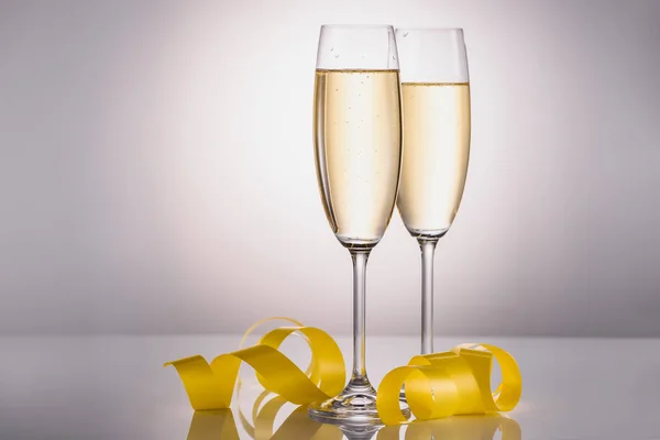 Close up view of glasses of champagne and yellow festive confetti on grey background — Stock Photo