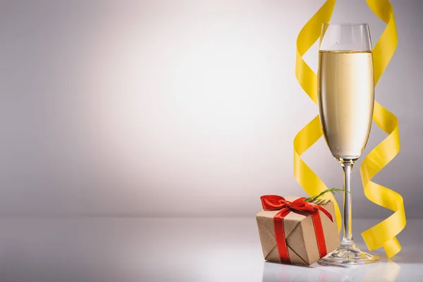 Крупним планом вигляд келиха шампанського і загорнутий різдвяний подарунок на сірому фоні — Stock Photo