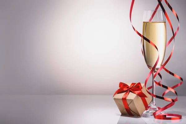 Close up view of glass of champagne and wrapped gift on grey backdrop — Stock Photo