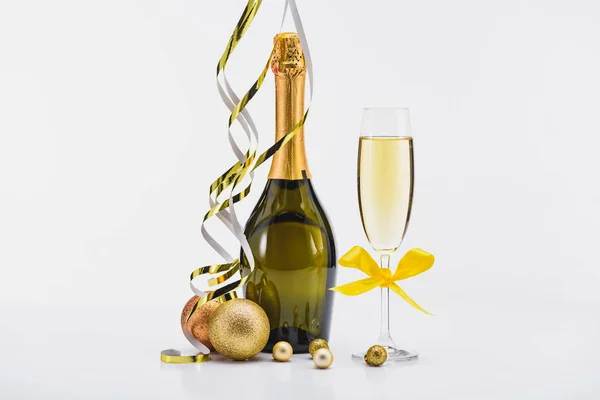 Закрыть вид на бутылку и бокал шампанского, конфетти и рождественские игрушки на белом фоне — стоковое фото