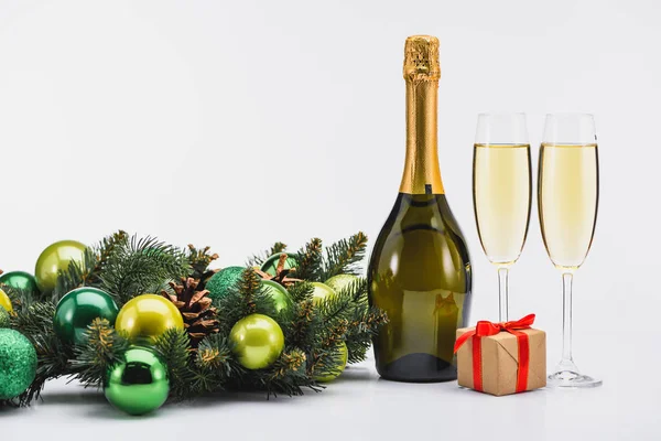 Vista de cerca de la botella y las copas de champán, corona de Navidad y regalo sobre fondo blanco - foto de stock