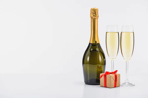 Vue rapprochée de la bouteille et des verres de champagne avec cadeau enveloppé sur fond blanc — Photo de stock