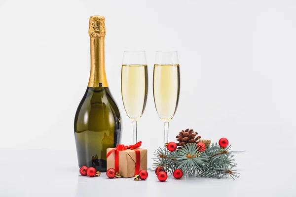 Vista de cerca de la botella y las copas de champán, decoraciones de Navidad y presente en el fondo blanco - foto de stock