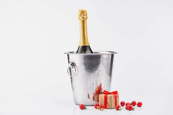 Крупним планом пляшка шампанського у відрі, різдвяні іграшки та загорнутий подарунок на сірому фоні — Stock Photo