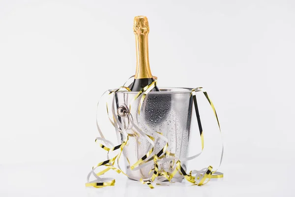 Vista de cerca de la botella de champán en cubo con guirnaldas festivas sobre fondo gris - foto de stock