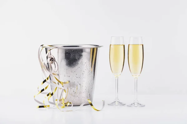 Vista de cerca de cubo, guirnaldas festivas y copas de champán sobre fondo gris - foto de stock