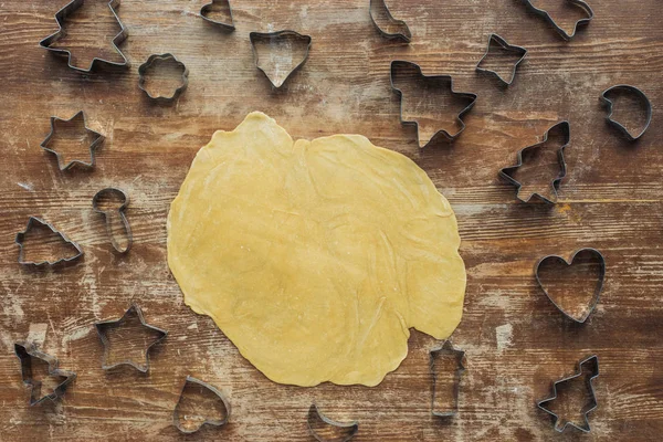 Yacía plana con masa cruda y cortadores de galletas de Navidad en la superficie de madera - foto de stock