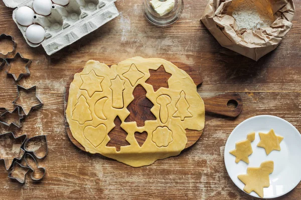 Flat lay with cut raw dough for christmas cookies baking on cutting board on wooden surface — Stock Photo