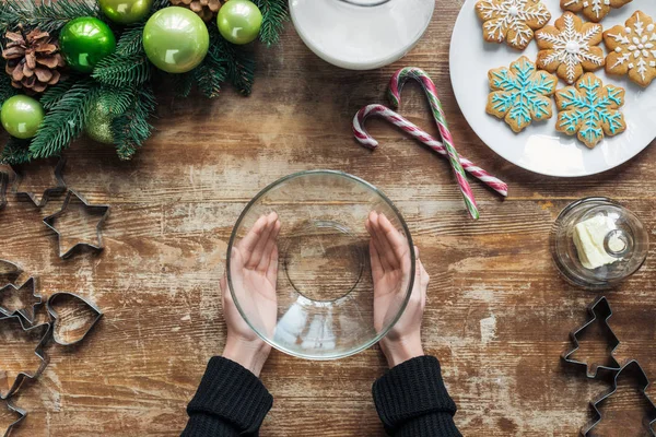 Teilansicht einer Frau mit leerer Schale auf Holzoberfläche mit Weihnachtskranz und Plätzchen — Stockfoto