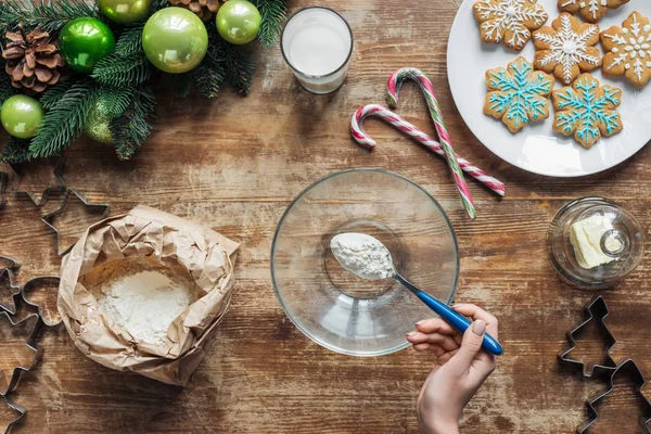 Plan recadré de femme versant de la farine dans un bol tout en faisant de la pâte pour les biscuits de Noël sur une table en bois avec une couronne décorative — Photo de stock