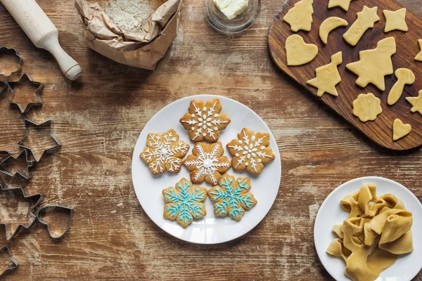 Flache Lage mit Weihnachtsplätzchen auf Teller, Zutaten und Ausstechformen auf hölzerner Tischplatte — Stockfoto