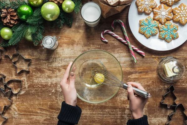 Abgeschnittene Aufnahme einer Frau mit Schneebesen, die Teig für Weihnachtskekse auf Holztischplatte mit dekorativem Kranz backt — Stockfoto