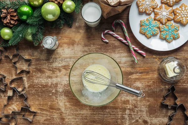 Vista superior de ingredientes misturados em tigela com batedor para biscoitos de Natal cozinhar na superfície de madeira — Fotografia de Stock