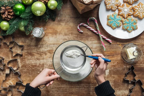 Tiro recortado de la mujer haciendo masa para galletas de Navidad panadería en mesa de madera con corona decorativa - foto de stock
