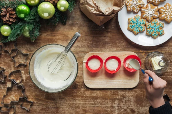 Teilansicht einer Frau, die Teig in Backformen auf hölzerner Tischplatte gießt, Weihnachtsbackkonzept — Stockfoto