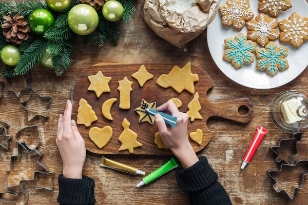 Vista parcial de la mujer decorando galletas de Navidad caseras con tinta de grado alimenticio en la superficie de madera - foto de stock