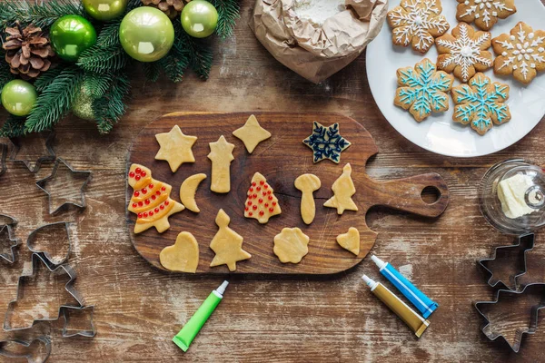 Ansicht der Anordnung von rohem Teig, lebensmittelechter Tinte für Weihnachtsgebäck und Weihnachtskranz auf hölzerner Tischplatte — Stockfoto