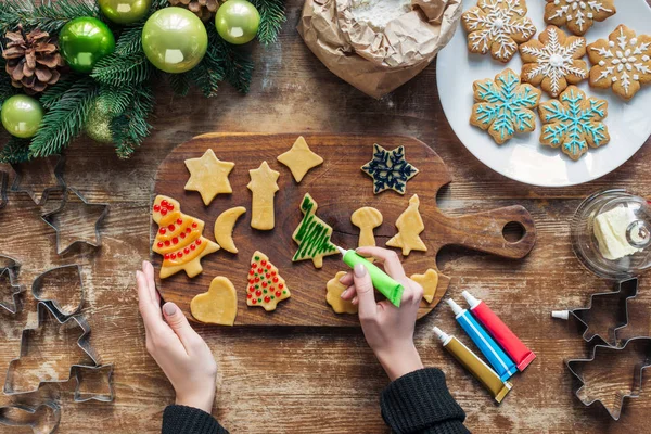 Vue partielle de la femme décorant les biscuits de Noël faits maison avec de l'encre de qualité alimentaire sur la surface en bois — Photo de stock