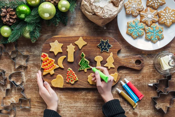 Vista parcial de la mujer decorando galletas de Navidad caseras con tinta de grado alimenticio en la superficie de madera - foto de stock