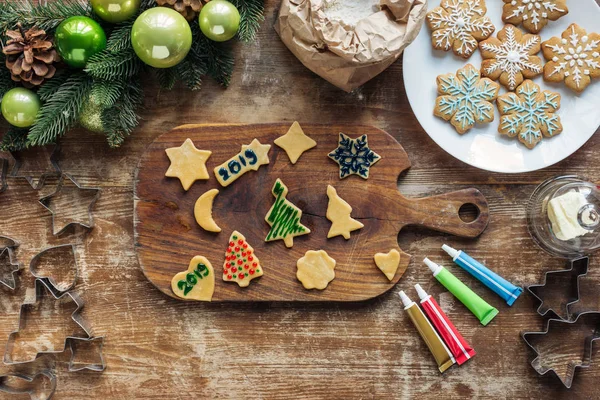 Vista superior de la disposición de la masa cruda, tinta de grado alimenticio para galletas de Navidad panadería y y corona de Navidad en la mesa de madera - foto de stock