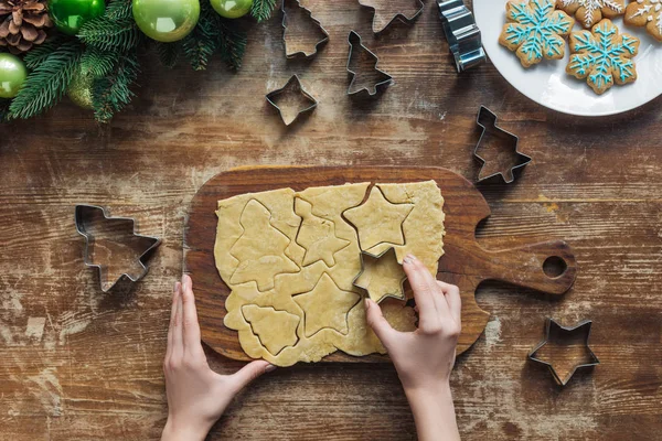 Tiro recortado de mujer cortando galleta de Navidad con cortador en mesa de madera con corona de Navidad decorativa - foto de stock