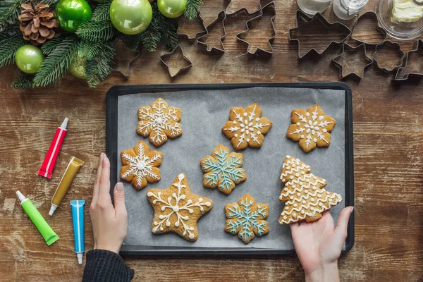 Partial view of woman holding baking pan with homemade christmas cookies on wooden surface — Stock Photo