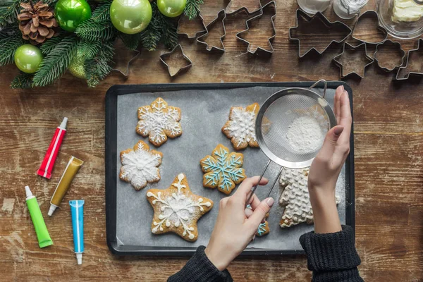 Vue partielle de la femme versant de la poudre de sucre sur les biscuits de Noël sur une plaque à pâtisserie — Photo de stock