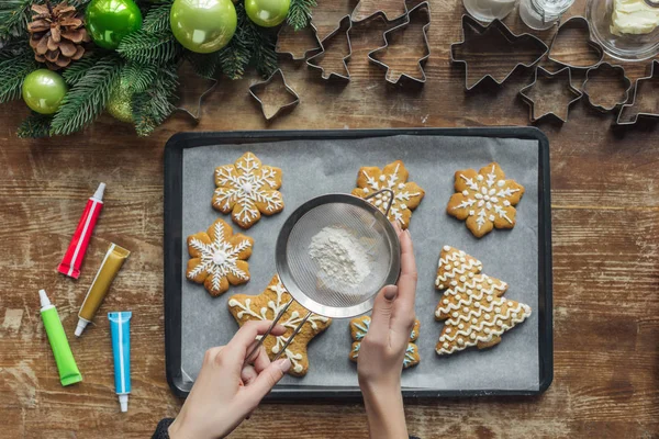 Teilansicht einer Frau, die Zuckerpuder auf Weihnachtsplätzchen auf Backform gießt — Stockfoto