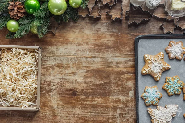 Cama plana con galletas de Navidad en bandeja para hornear, corona de Navidad, caja de cartón y cortadores de galletas en la superficie de madera - foto de stock
