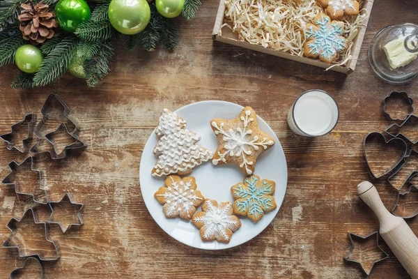 Posa piatta con biscotti al forno sul piatto su superficie di legno con corona decorativa natalizia e vetro di latte — Foto stock