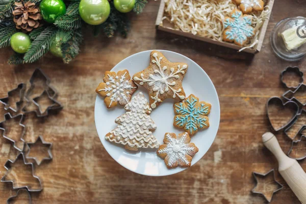 Flache Lage mit gebackenen Plätzchen auf Platte auf Holzunterlage mit weihnachtlichem Dekorationskranz und Nudelholz — Stockfoto