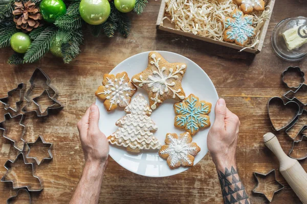 Cropped shot of man holding plate with homemade christmas cookies on wooden surface — Stock Photo