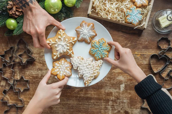 Foto recortada de amigos sosteniendo galletas de Navidad caseras en el plato en la superficie de madera - foto de stock