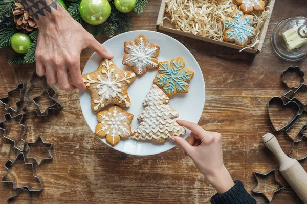 Vista parcial del hombre y la mujer sosteniendo galletas caseras en la mesa de madera con corona decorativa de Navidad - foto de stock