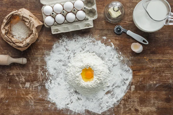 Top view of white flour pile with egg and baking ingredients on wooden table — Stock Photo