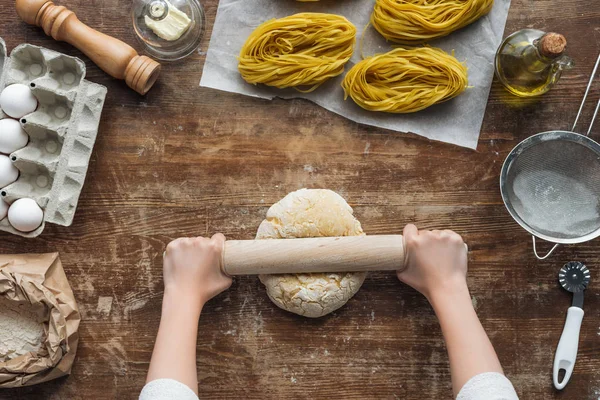 Top view of female hands forming dough with rolling pin on wooden table — Stock Photo