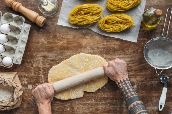 Vue de dessus des mains masculines formant la pâte avec rouleau à pâtisserie sur table en bois — Photo de stock