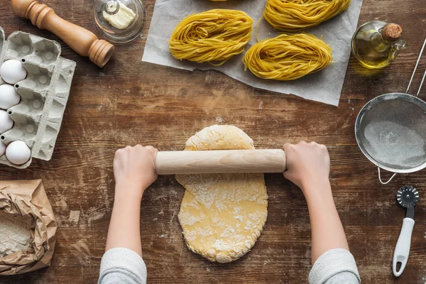Vue de dessus des mains féminines formant la pâte avec rouleau à pâtisserie sur table en bois — Photo de stock