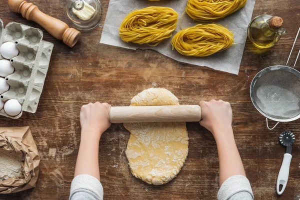 Vista superior de las manos femeninas formando masa con rodillo sobre mesa de madera — Stock Photo